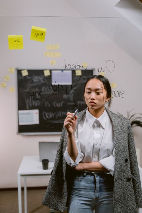 Free Businesswoman writing on glass board during meeting in a modern office setting. Stock Photo