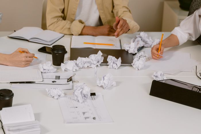 Hands working over a table of notes and crumpled paper, photo by Tima Miroshnichenko on Pexels