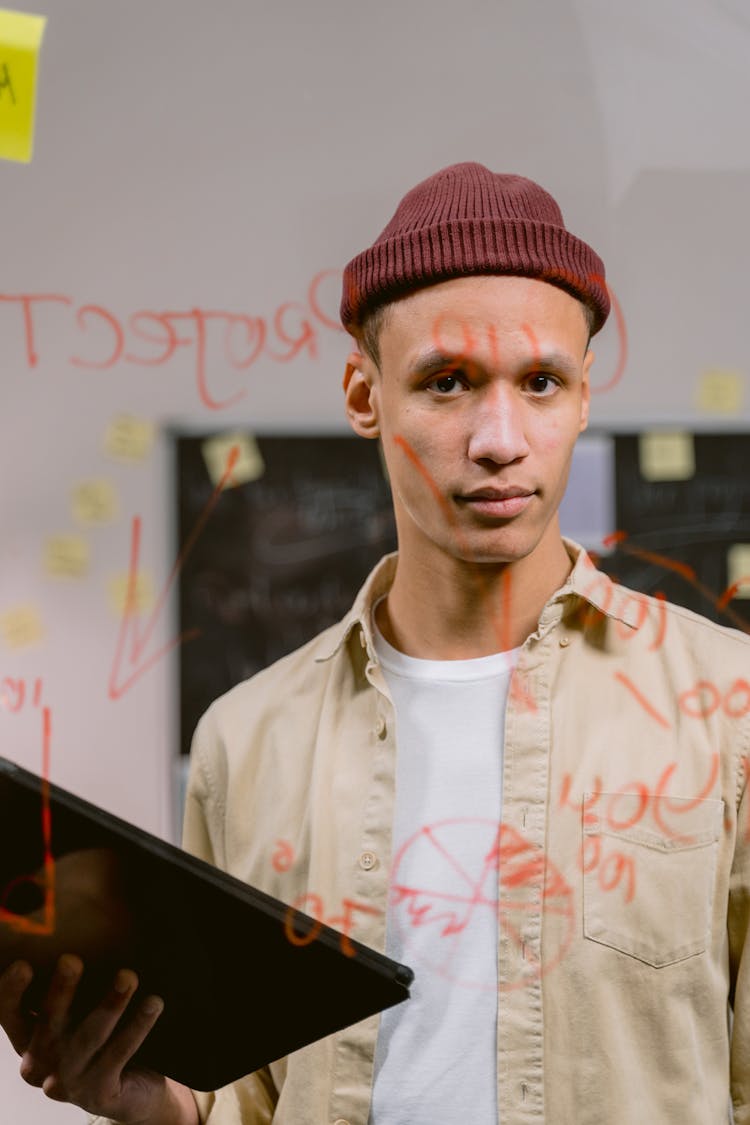 Young Man In Red Beanie Holding A Tablet Standing In Front A Transparent Glass