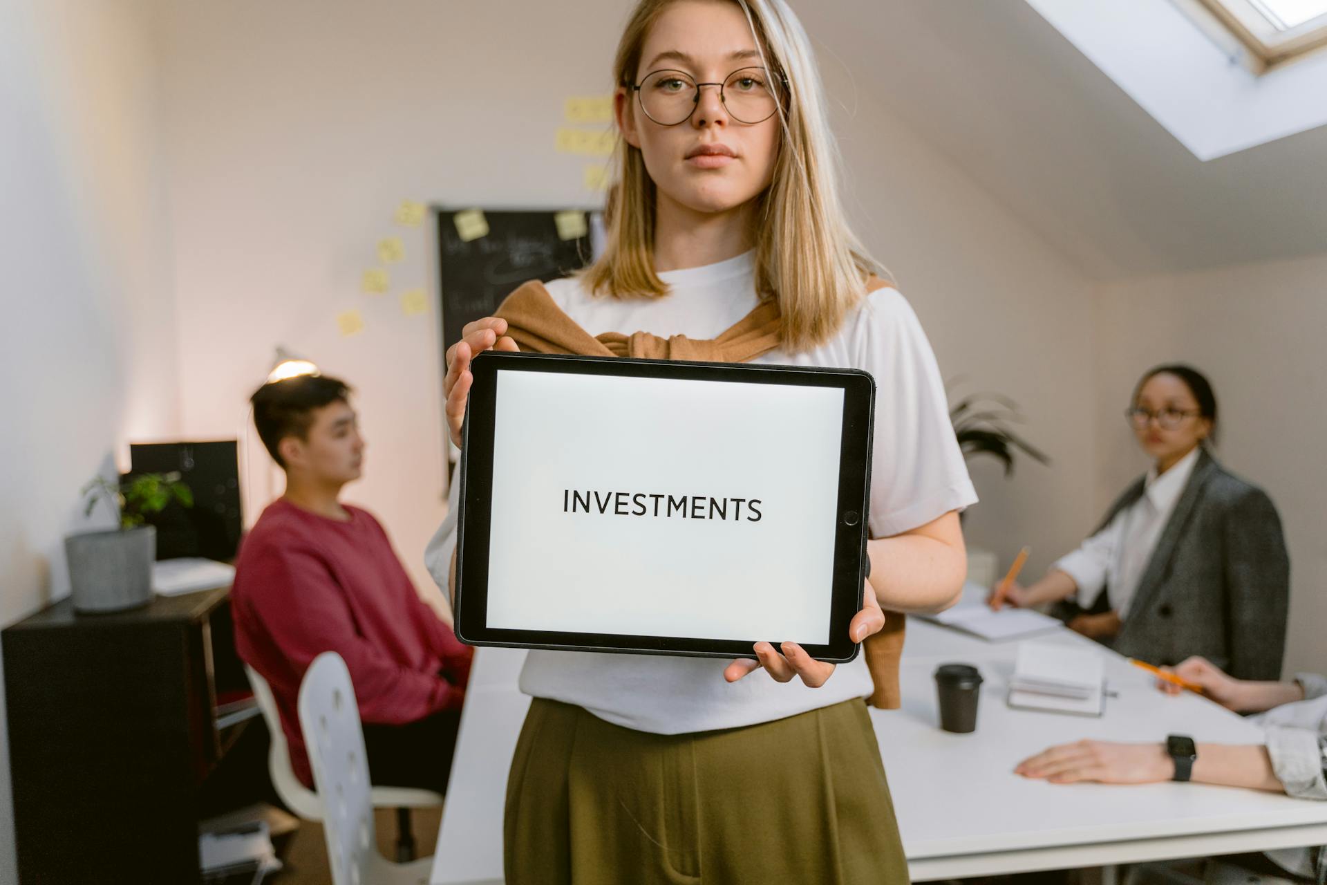 Young professional holding tablet in team meeting focused on investments.