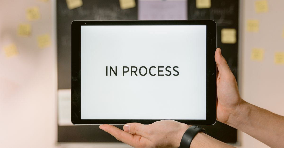 Photo by Tima Miroshnichenko Close-up of hands holding a tablet displaying 'In Process' text, emphasizing workflow.
