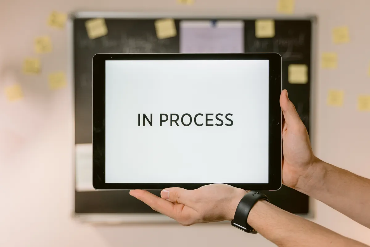 Hands holding a tablet displaying 'IN PROCESS