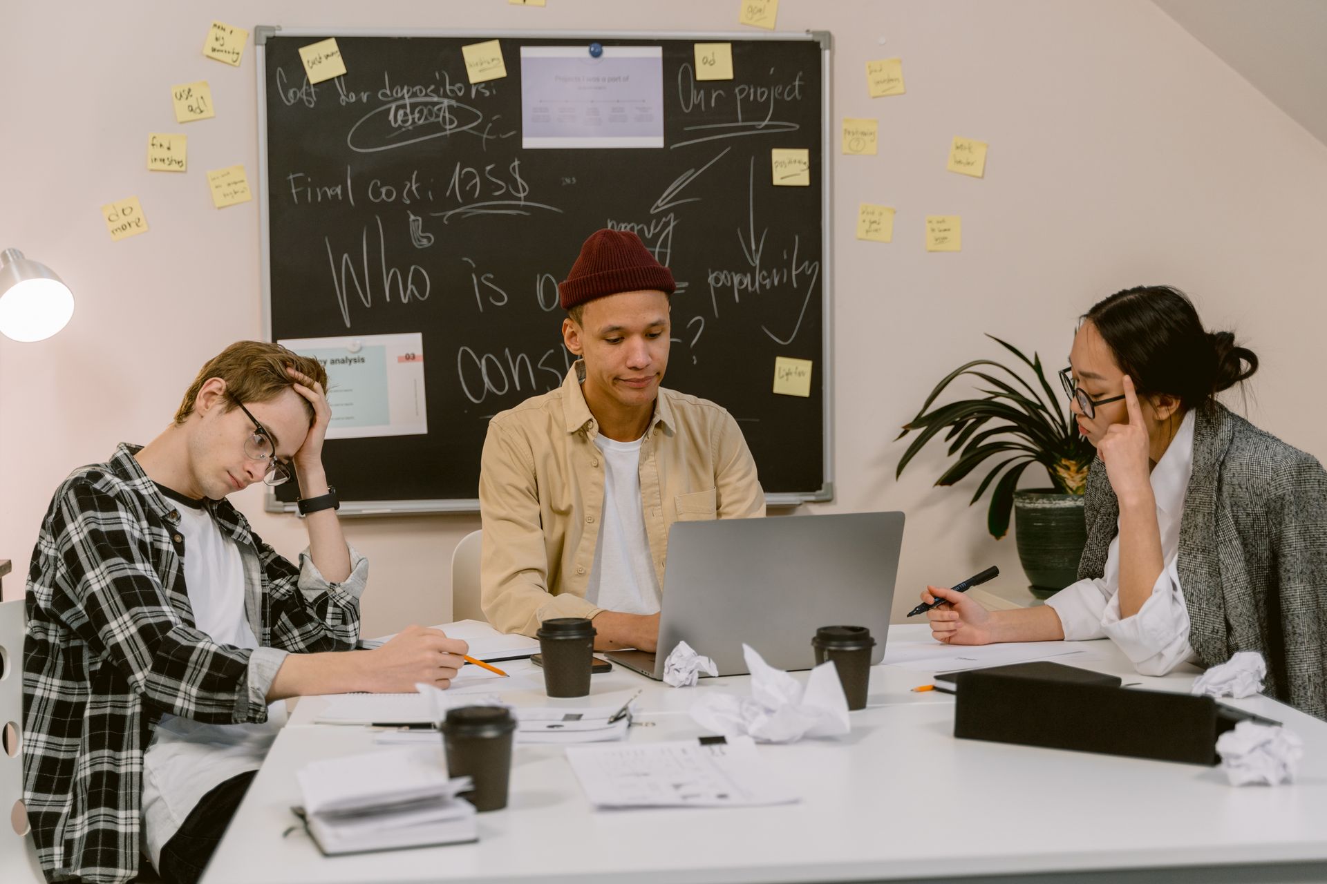 College students brainstorming around a table, studying with laptops and notes.
