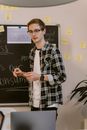 Man in Black and White Plaid Dress Shirt Standing Near Black Chalk Board