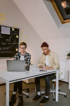 Two young men brainstorming and working together at a desk in a modern office setting.
