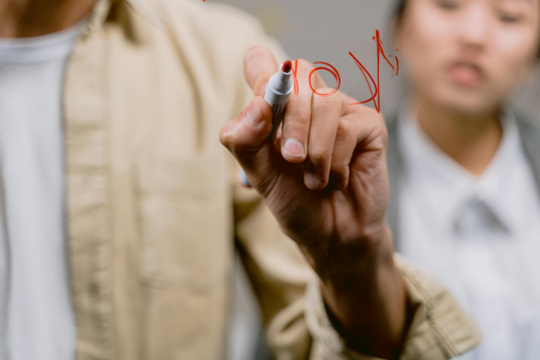 A person writing on a glass panel with red marker in an office setting.