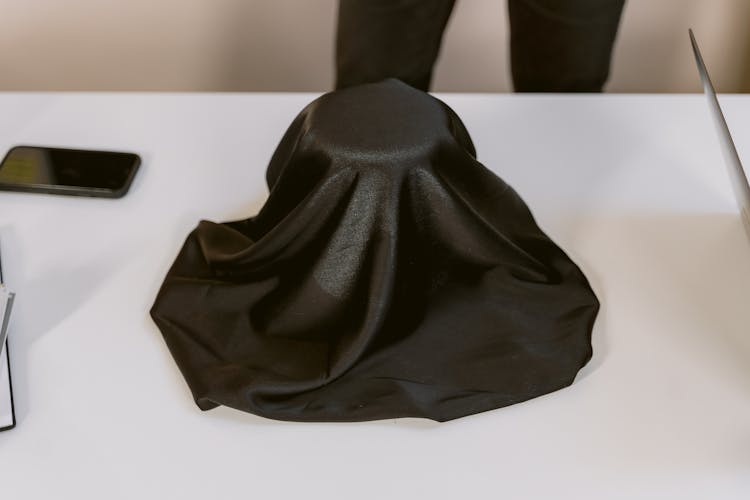 A Black Cloth Covering An Object On A White Surface