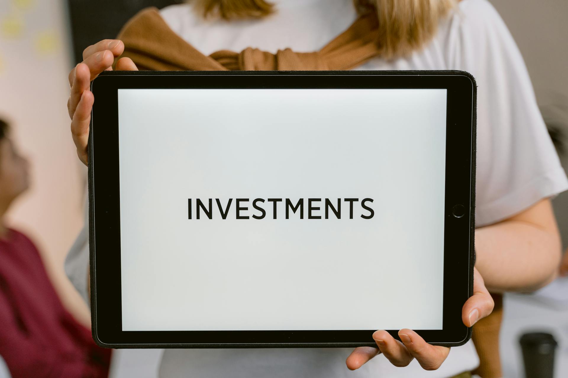 Close-up of a tablet with the word 'Investments', held by a person. Ideal for financial topics.