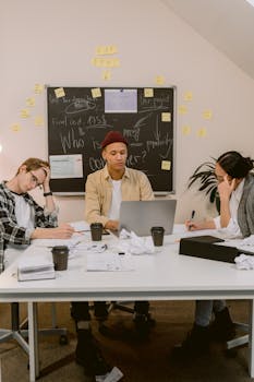 Diverse team collaborating in office, brainstorming ideas on laptop and blackboard.