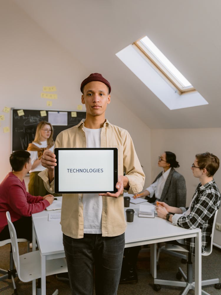 A Man In Beige Long Sleeves Holding A Tablet While Standing Near His Colleagues