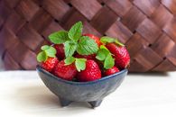 Vibrant fresh strawberries with mint leaves in a black ceramic bowl. Perfect for healthy eating concepts.