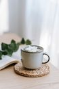 Cup of green hot beverage with blossoming white flower on straw mat against book in house