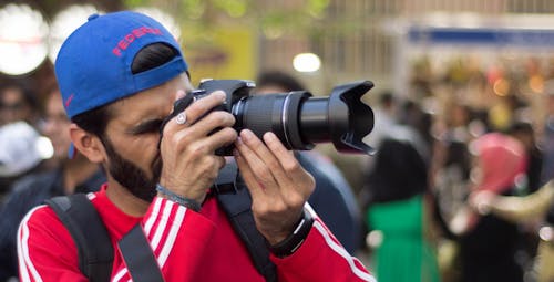 無料 黒のカメラ本体を保持している赤と白のクルーネック長袖シャツの男 写真素材