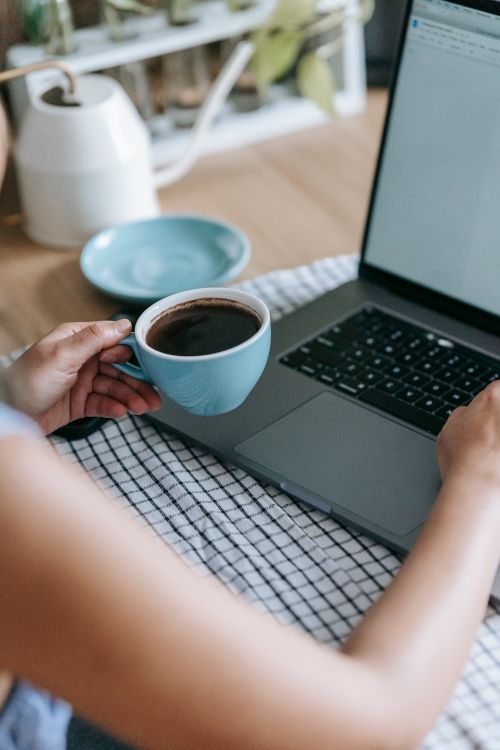 Free From above of crop unrecognizable female using netbook and drinking mug of coffee at home Stock Photo