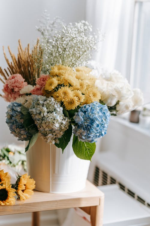 Lush composition of multicolored flowers in vase on wooden table against blurred background