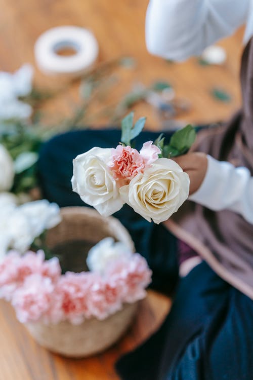 Free From above of crop anonymous florist with blooming roses sitting on floor white arranging flowers on wicker flowerpot on blurred background Stock Photo