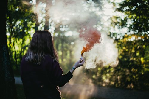 Free A woman in a forest holding a vibrant orange smoke bomb during daylight. Stock Photo