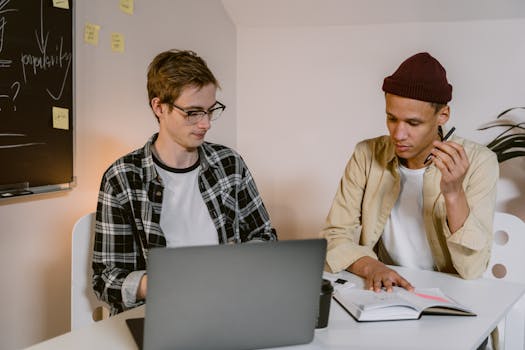 Two young colleagues working together at a laptop in a modern office setting.