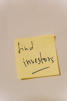 Close-up of a handwritten note reminding to find investors, on a wall.