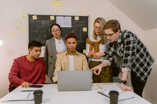 A diverse group of colleagues engaging in a collaborative office meeting with a laptop.