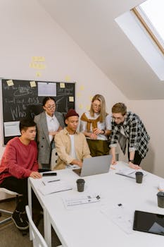 Diverse team brainstorming in a modern office setting around a laptop.