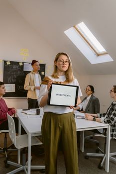 Confident young woman displaying an investment concept on a tablet in a modern office setting.