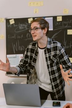 Motivated young man conducting a business presentation in an office with a blackboard and laptop.