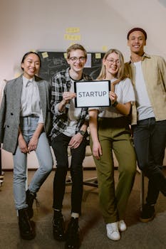 A diverse group of young adults standing confidently with a startup sign in an office setting.
