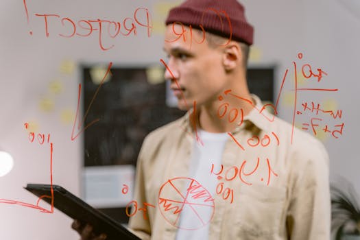 Man strategizing ideas on a glass panel with red marker writings, creating an innovative brainstorming session.