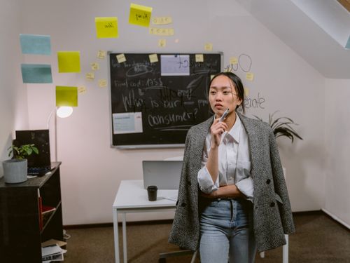 Free A thoughtful woman in an office, brainstorming ideas by a chalkboard with sticky notes. Stock Photo
