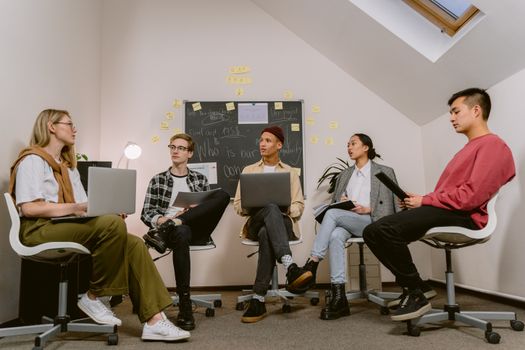 Young professionals engage in a collaborative meeting with laptops and a chalkboard focus.