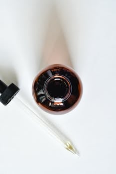 Close-up view of a brown glass bottle with a pipette on a white background.