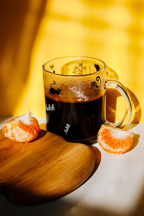 Free Glass of hot aromatic coffee with halved tangerine near chopping board in sunlight Stock Photo