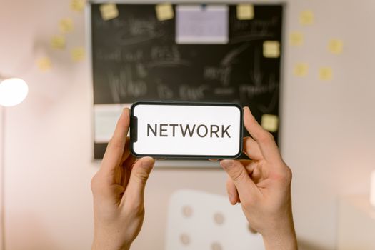 Hands holding a smartphone with 'NETWORK' text on screen, concept of digital communication.