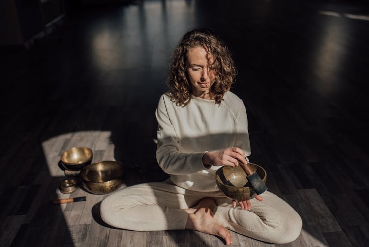 Spiritual Practitioner Playing Bowl Gong On Floor In Sunlight