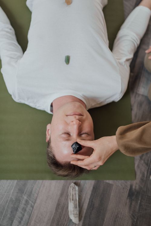 Free Man lying on mat with healing minerals, receiving a relaxing crystal therapy session indoors. Stock Photo