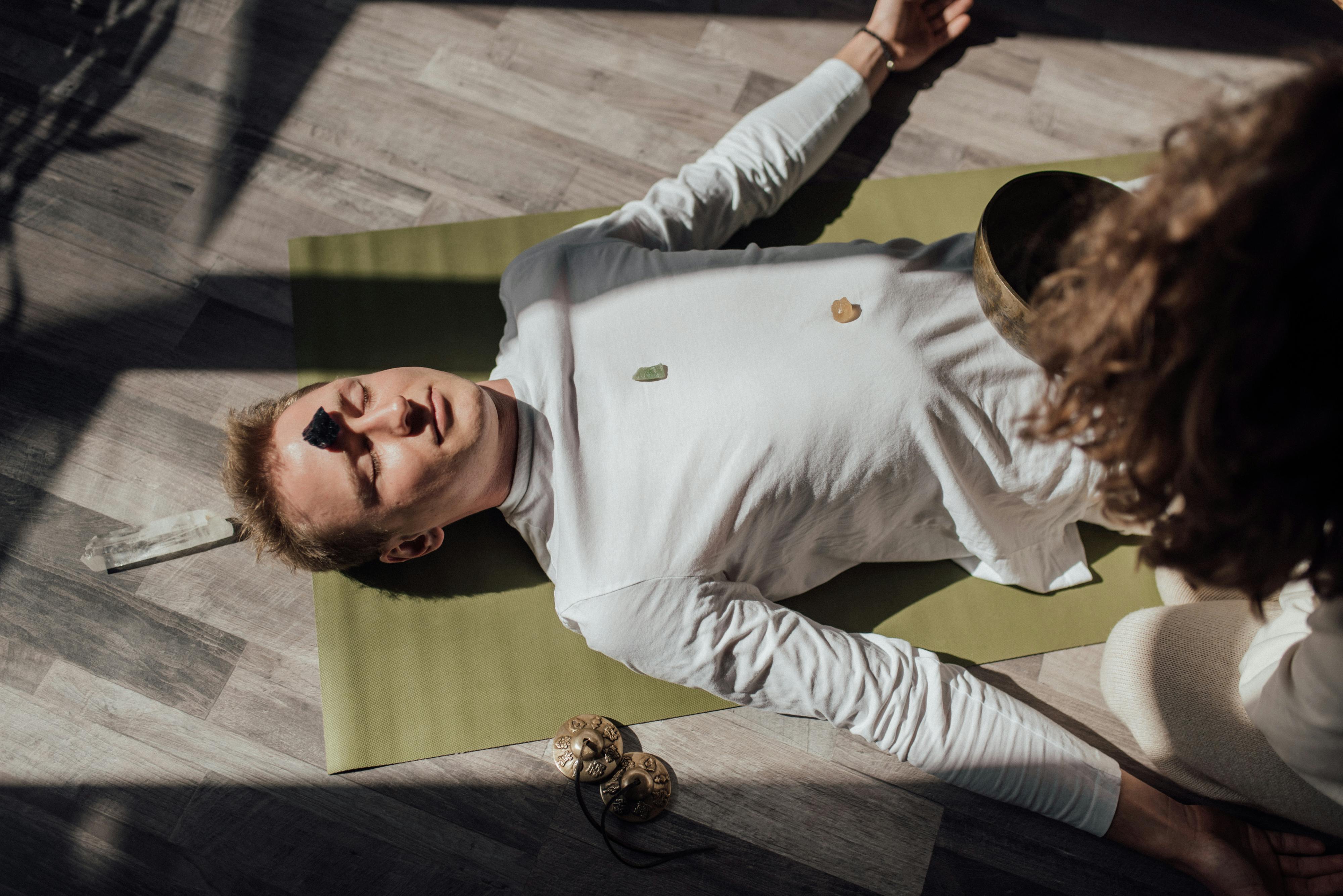 Man lying on yoga mat with healing crystals during meditation for relaxation and balance.
