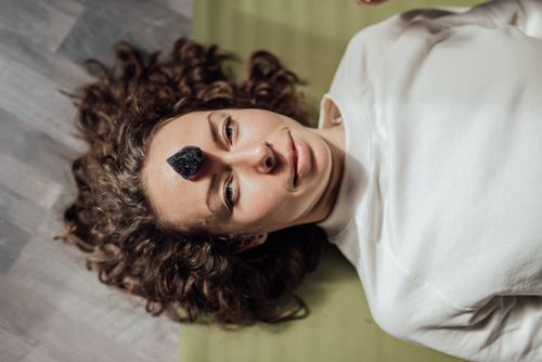 Free Young woman lying down with a healing crystal on her forehead, promoting relaxation and meditation. Stock Photo