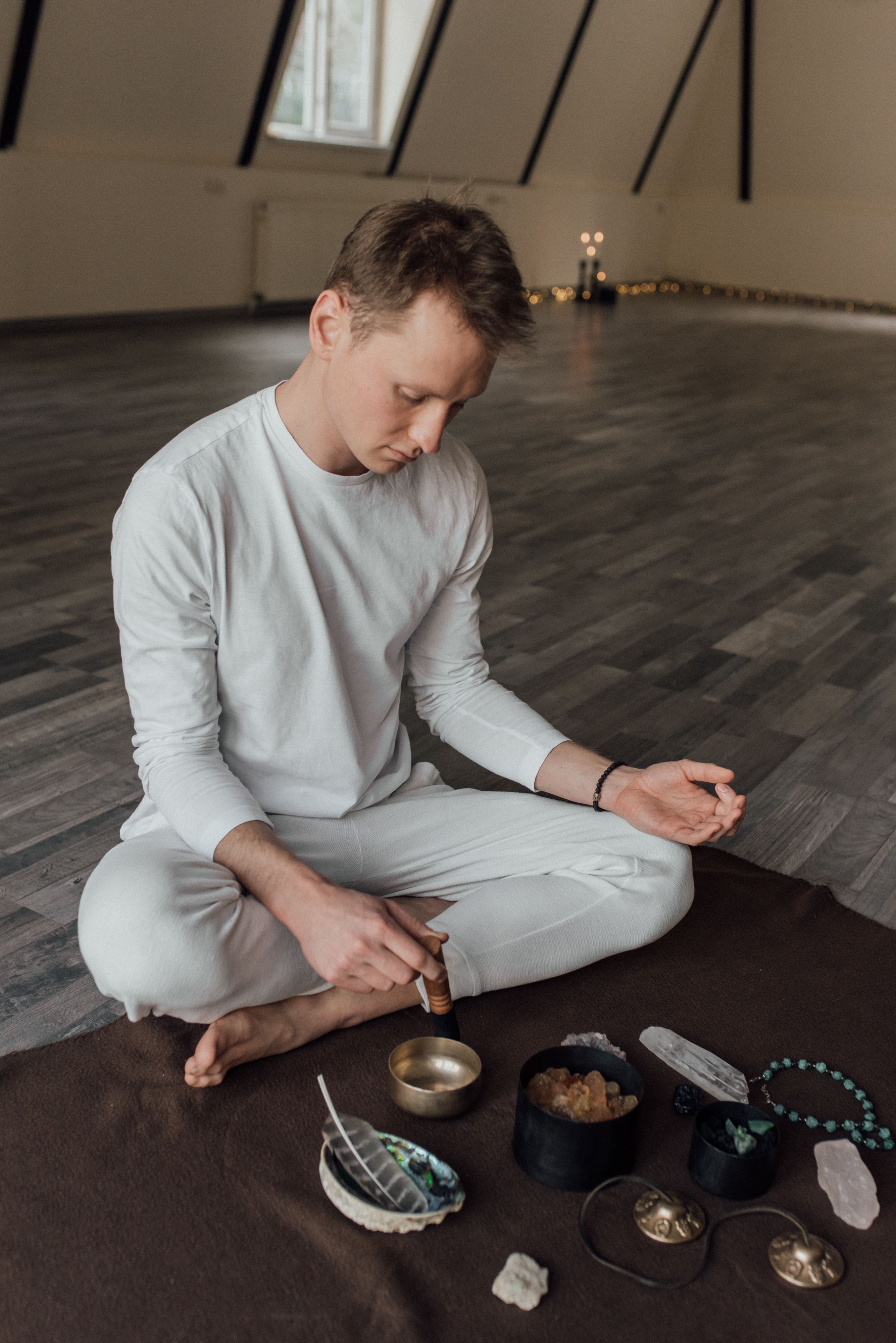 Man in white meditates with Tibetan singing bowl, enhancing calmness in a serene indoor space.