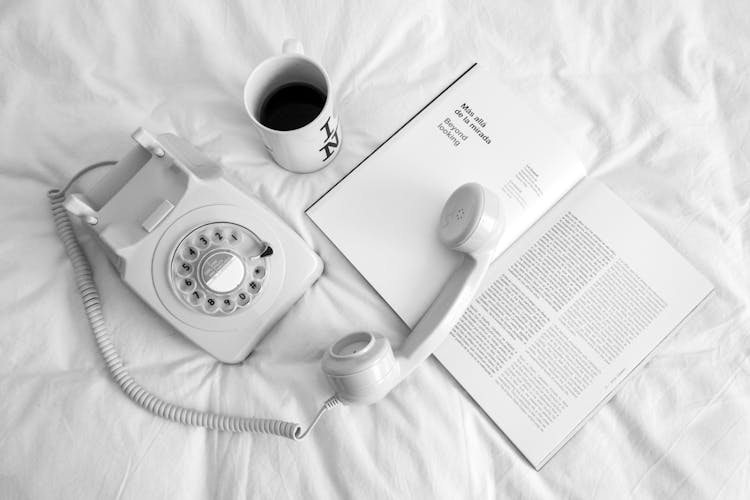 White Rotary Phone Beside A White Ceramic Mug