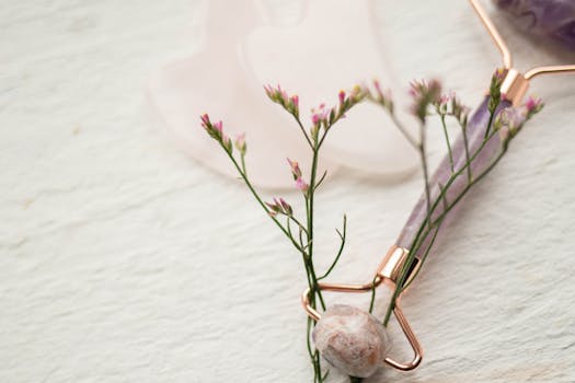 Aesthetic composition featuring a cosmetic roller and delicate pink flowers, ideal for beauty and wellness themes.