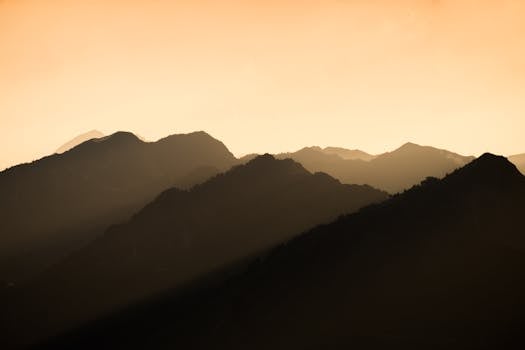 Stunning silhouette of mountains during a vibrant sunset with warm orange hues.