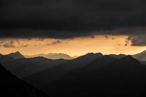 Free Captivating view of mountain silhouettes beneath a dramatic cloudy sunset sky. Stock Photo