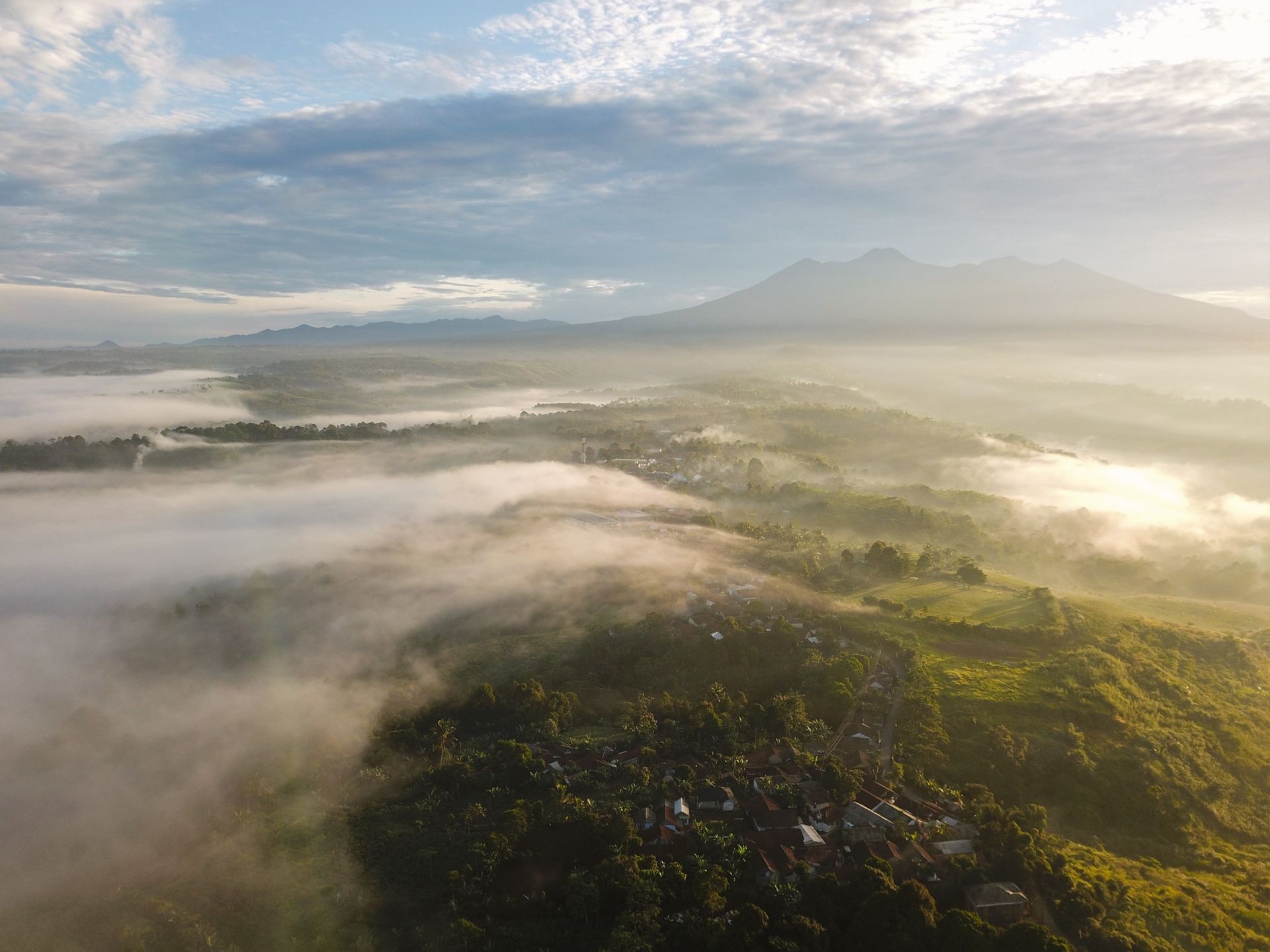Stunning aerial view showcasing mist over a rural landscape with mountains in the background.