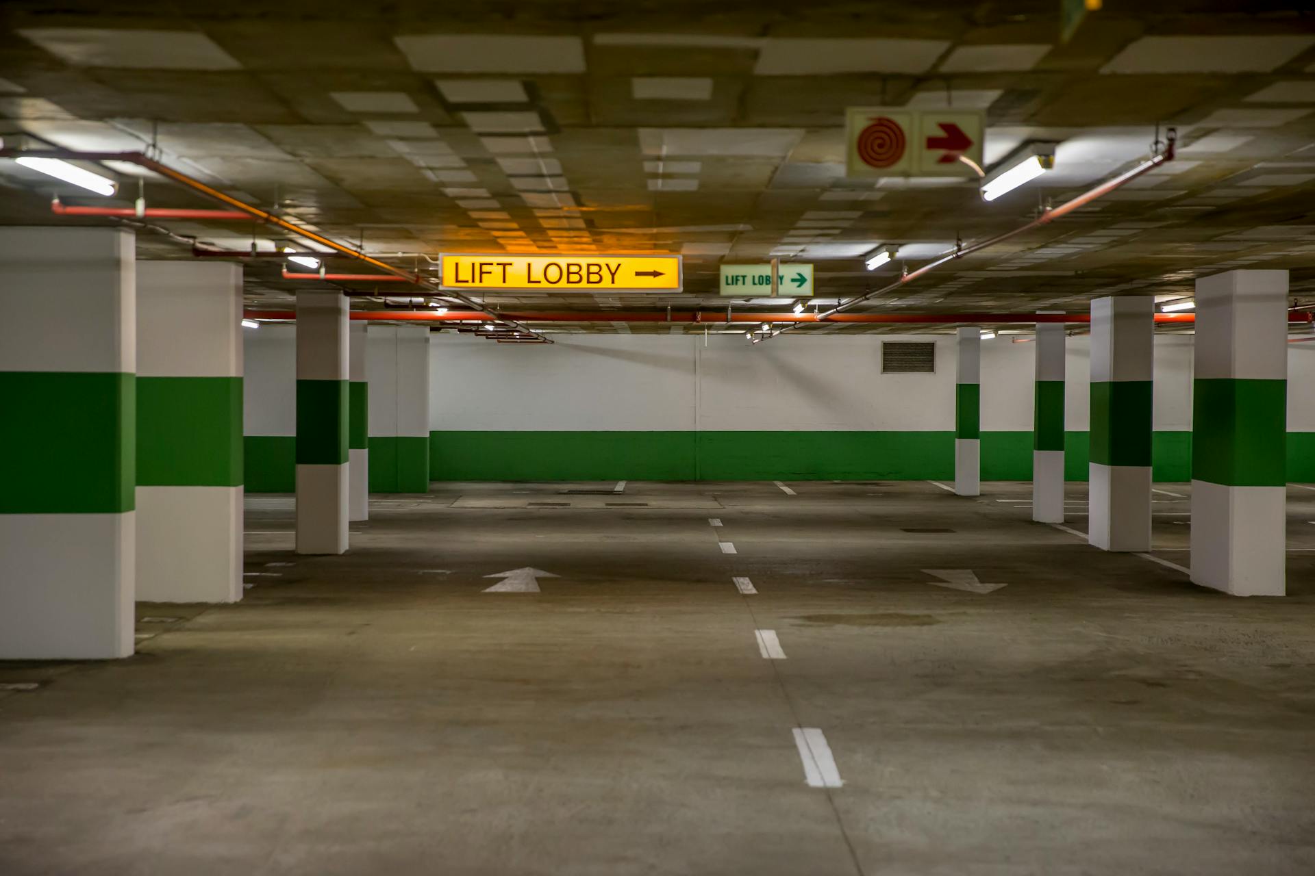 Empty underground parking garage with visible lift lobby sign and green accents.