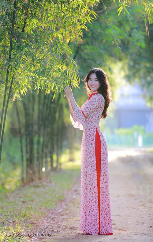 Free Woman in Red and White Floral Dress Standing Under Green Tree Stock Photo