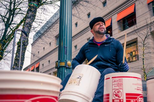 Free Low angle of bearded male in casual clothes and cap drumming on plastic buckets while sitting on city street in autumn Stock Photo