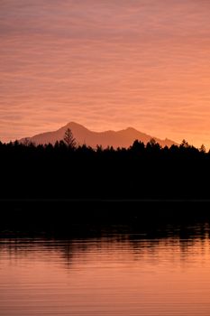 A tranquil mountain silhouette at sunset with vibrant orange sky reflecting on the lake.