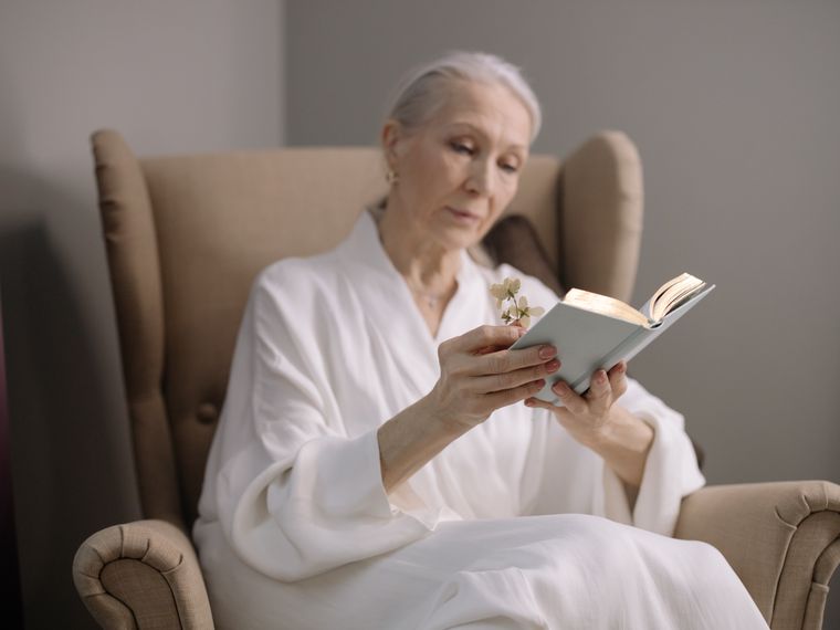 An elderly woman reading a book in an armchair at home.