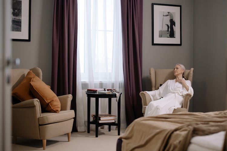 Elderly Woman In White Robe Sitting On Sofa Chair